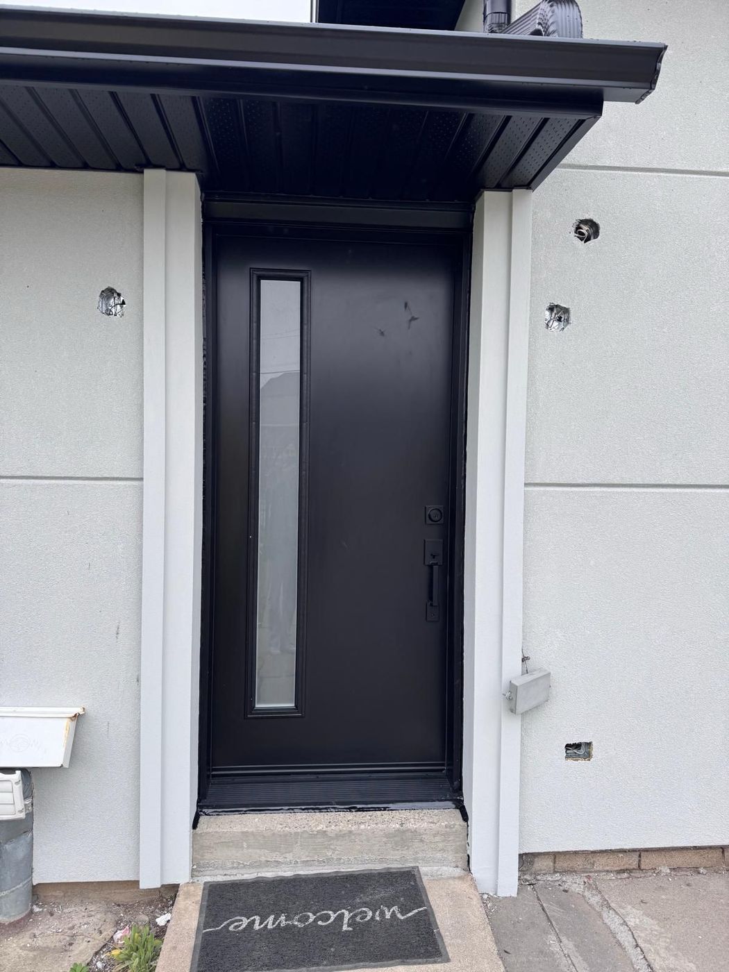 Black modern entrance door with a narrow vertical glass sidelite under a black steel portico