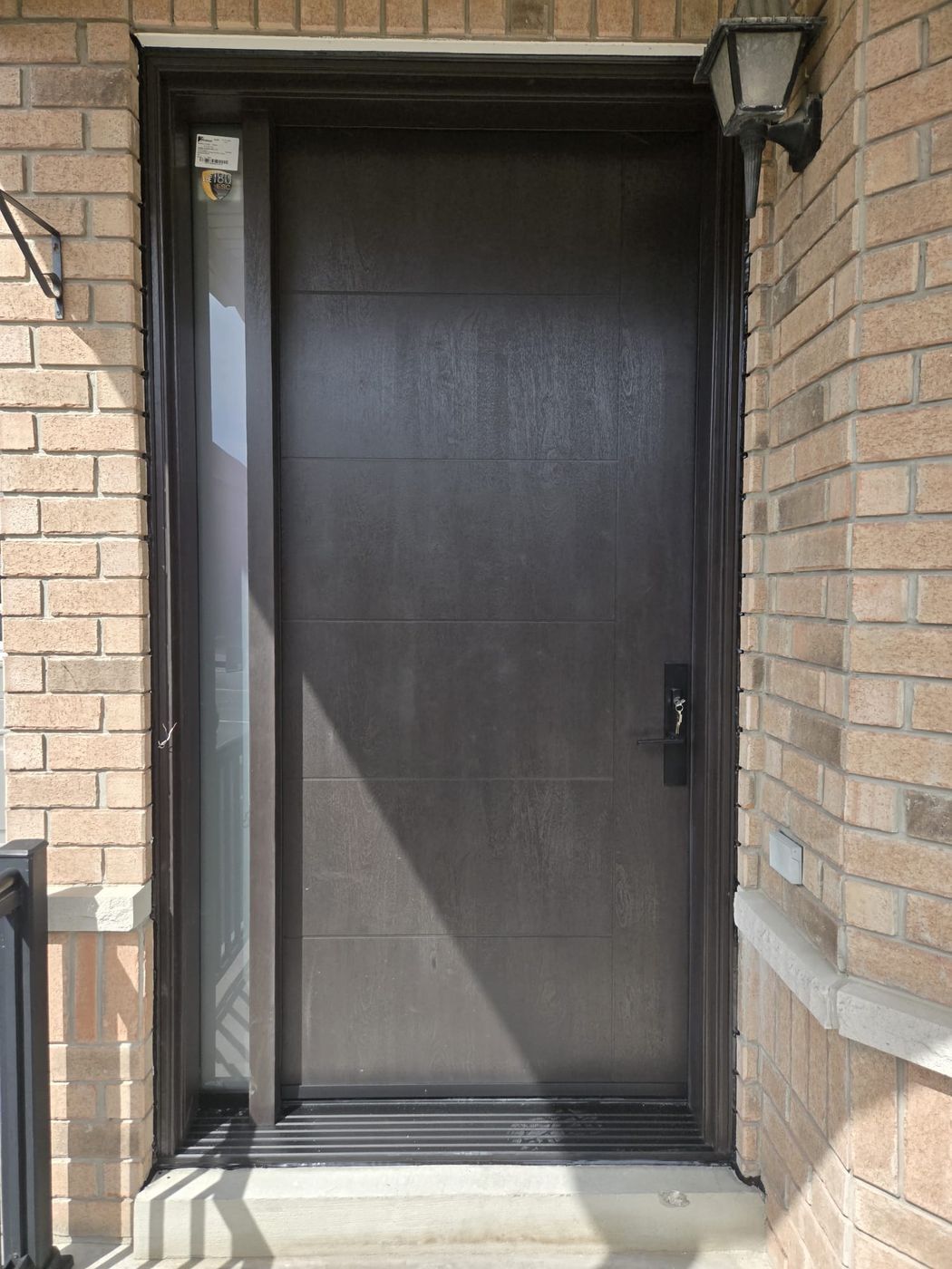 Espresso woodgrain fibreglass entrance door with sidelite, the Cardinal Low-E 180 ESC glass label still attached after installation by Royalty Doors and Windows