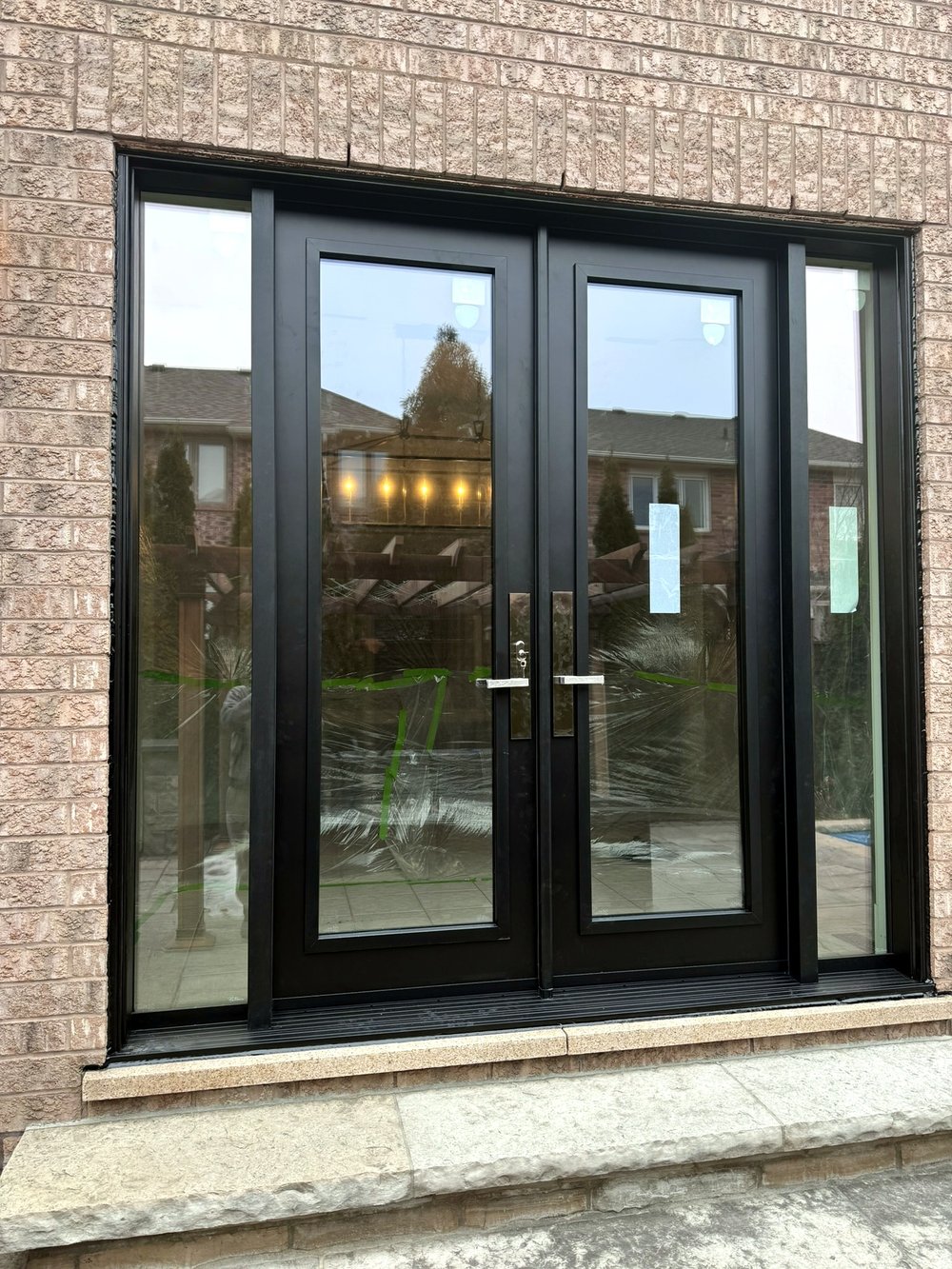 Black double patio doors with full glass panels on a stone home exterior