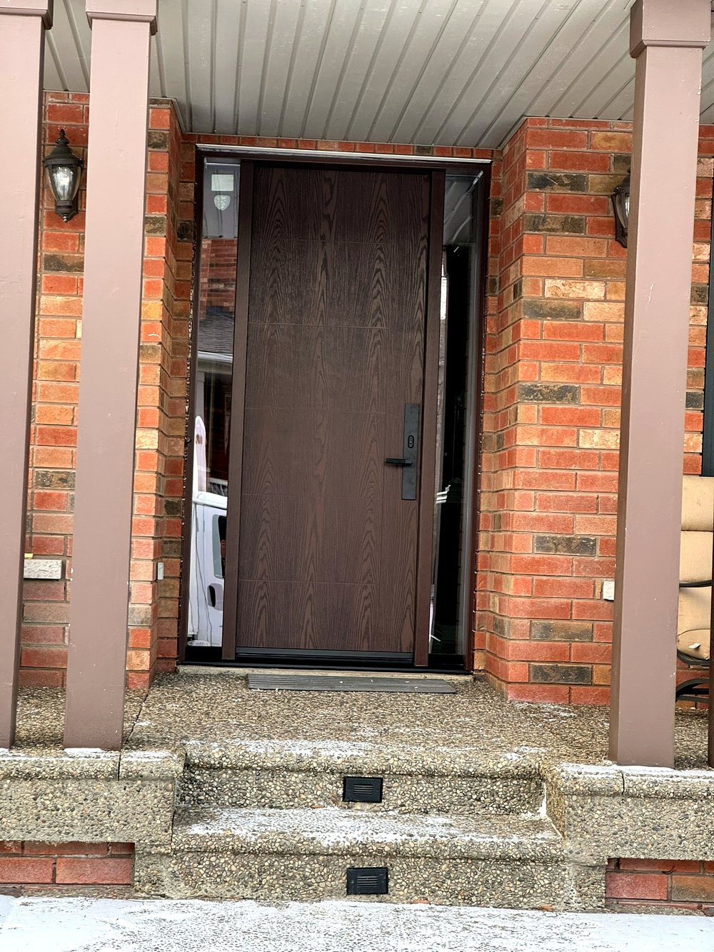 Bronze wood-grain entrance door with sidelight glass on a brick home