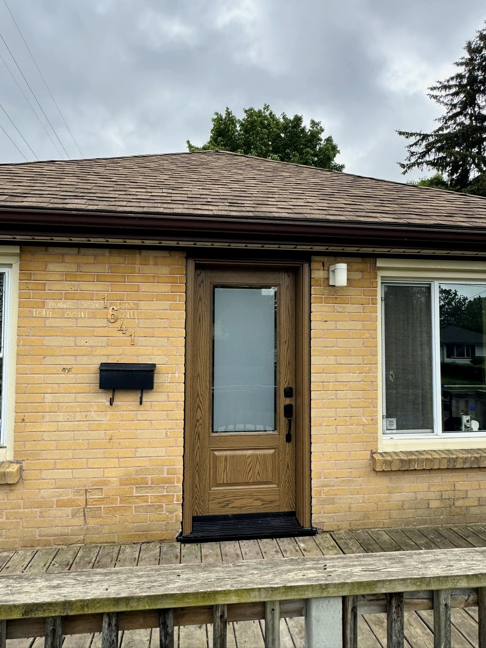 Oak wood-grain entrance door with full glass panel on a brick bungalow