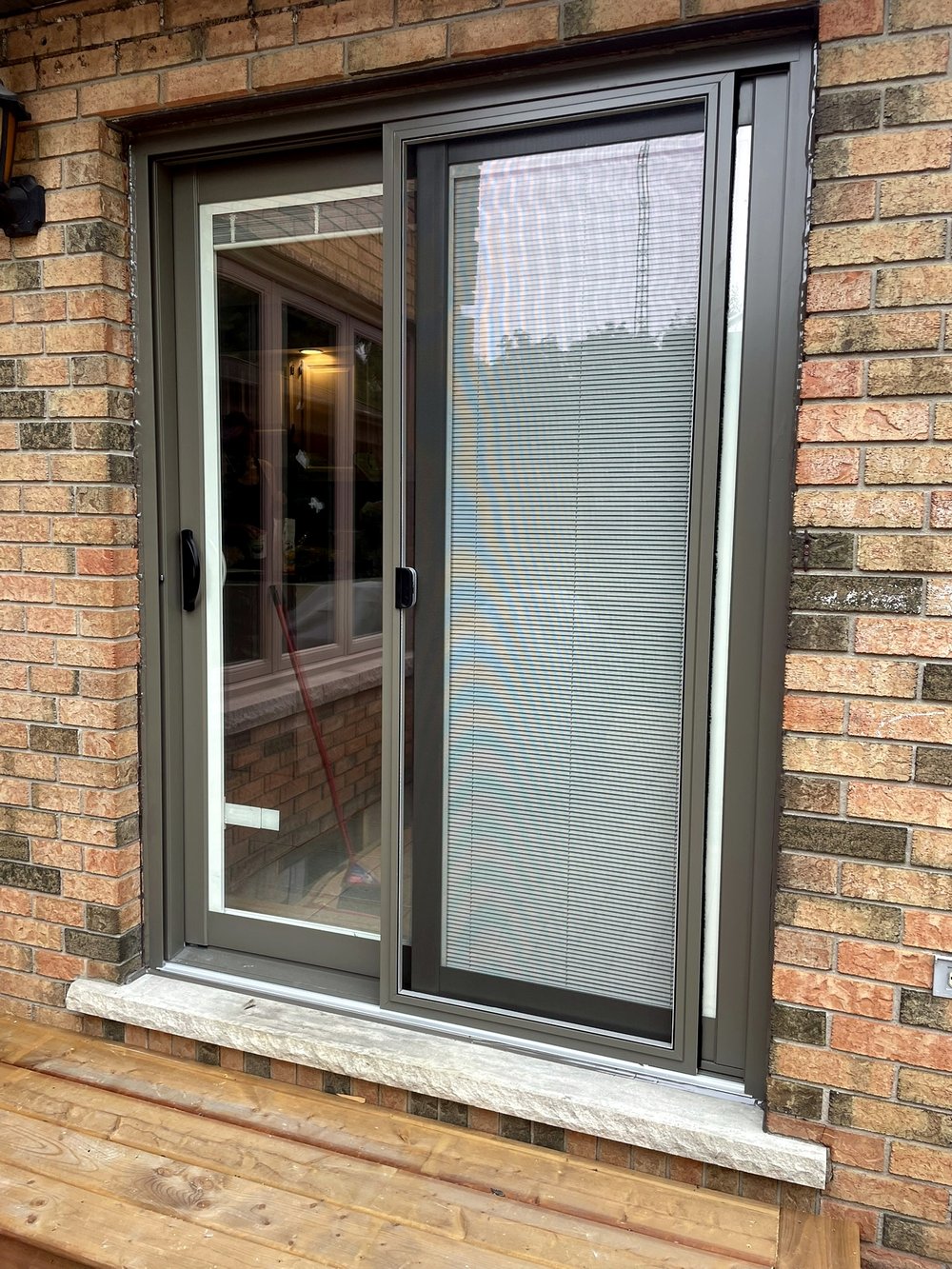 Bronze-framed sliding patio door with privacy blinds on a brown brick home