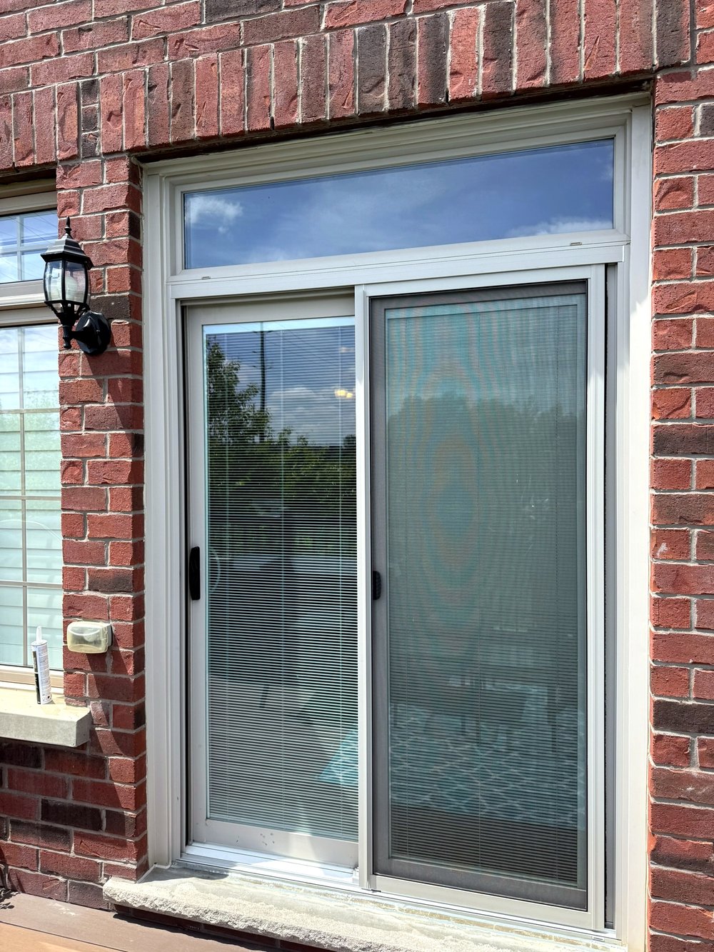 White-framed sliding patio door with transom window on a red brick home