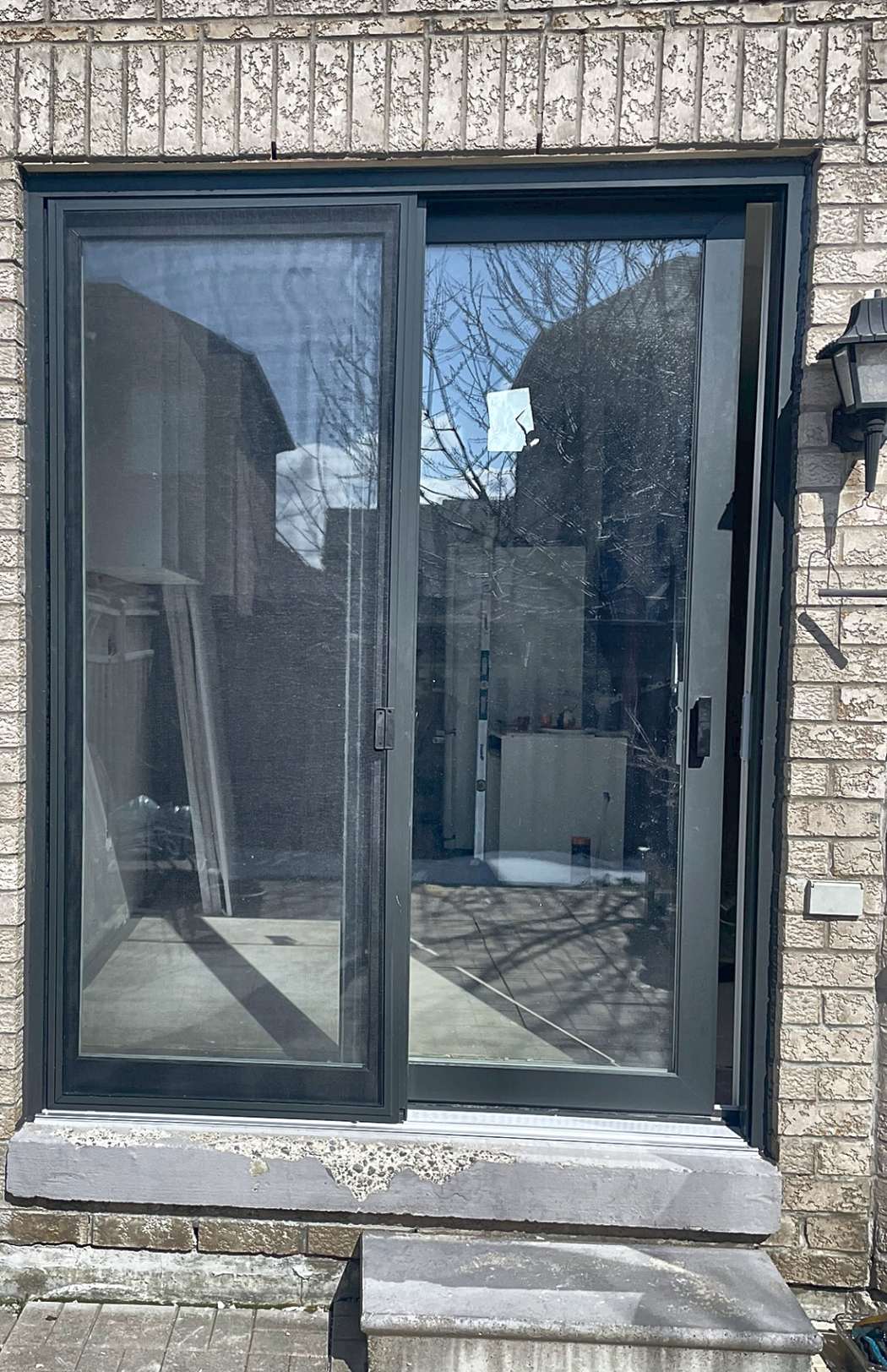 Charcoal grey Vista sliding patio door with retractable screen installed in a beige brick home by Royalty Doors and Windows