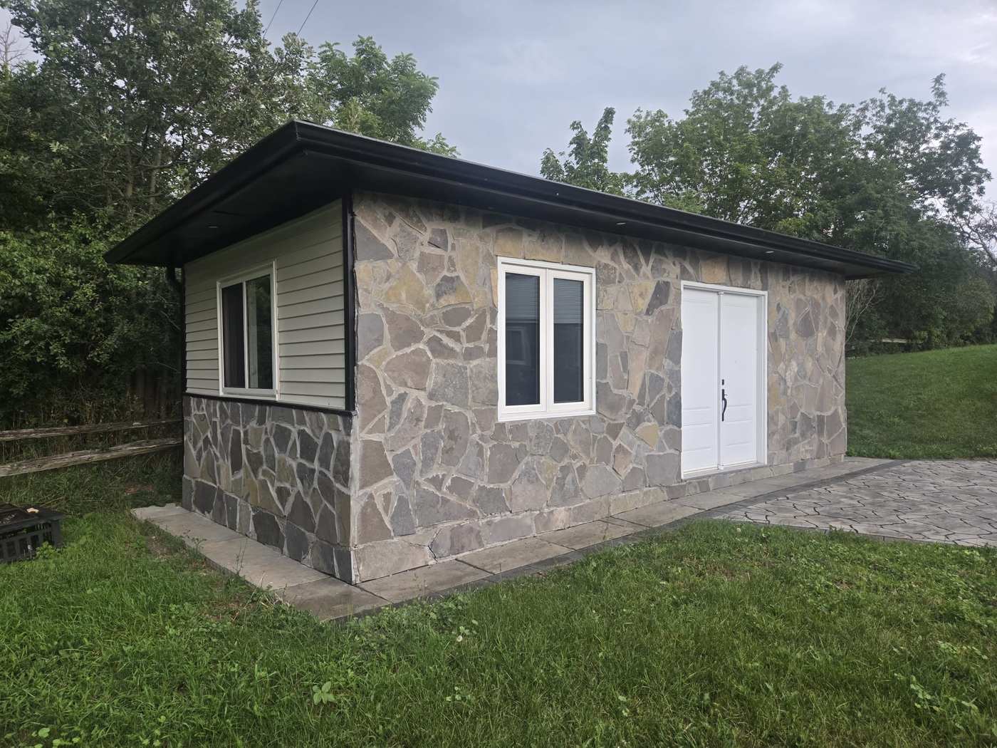 Side view of a stone and vinyl-sided garden building with new white slider windows and double doors installed by Royalty Doors and Windows