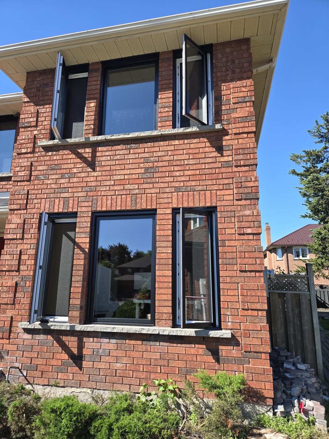 Black-framed vinyl casement windows standing open on a red brick Toronto home, installed by Royalty Doors and Windows