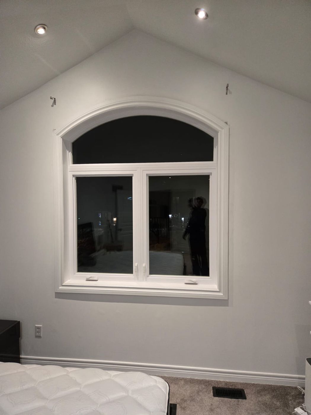 Interior view of white vinyl casement windows with an arched transom in a vaulted-ceiling bedroom, installed by Royalty Doors and Windows